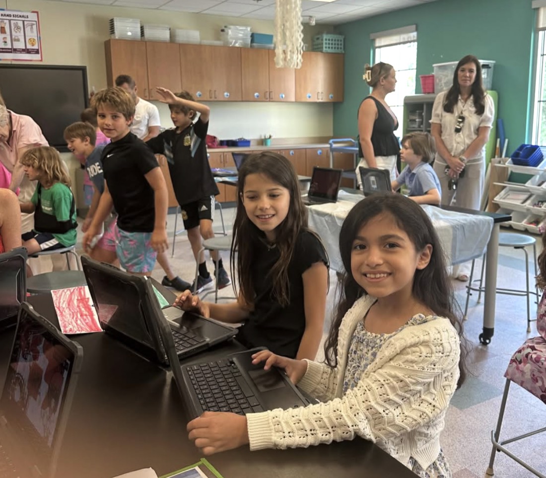 Students smile while working on laptops in a bright SIES classroom